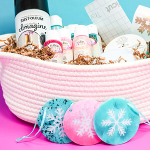 Pink and blue ornaments with snowflakes on them in front of a basket full of Rust-Oleum and Testors paints and other craft supplies.