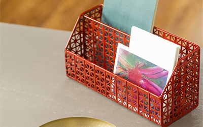 A red metal desk caddy containing a notebook, envelopes and cards.
