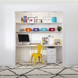 A closet office with shelves, a computer and a bright yellow chair.
