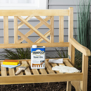 Can of Watco Teak Oil with sandpaper on an unfinished wood bench.