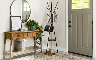 Entryway of a home with a light fixture, coat rack and mirror over a table with a potted plant and framed picture sitting on top.