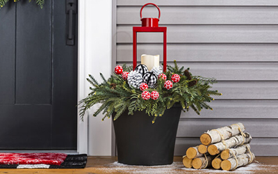 Black planter filled with greenery, pine cones and a red lantern.