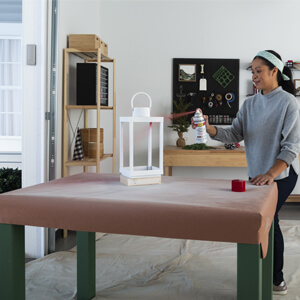 A woman applying spray paint to a white decorative lantern.
