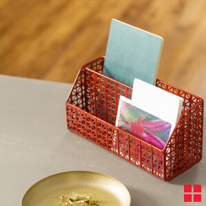 A red metal desk caddy containing a notebook, envelopes and cards.