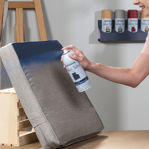 Spraying blue Rust-Oleum Outdoor Fabric Paint onto a gray patio cushion.