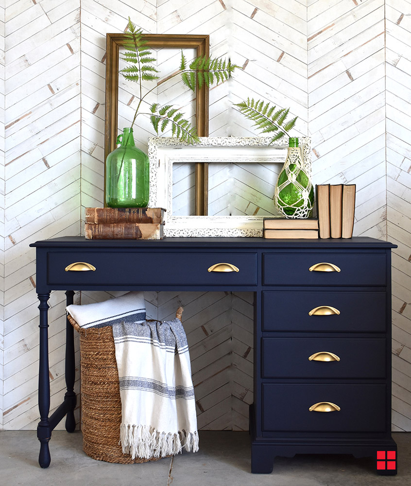 Navy blue desk with gold drawer handles, and books, vases and frames on top.