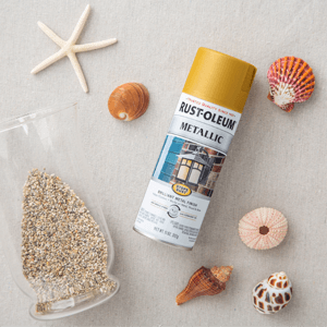 Can of Rust-Oleum Metallic Spray Paint beside shells and a vase with sand.