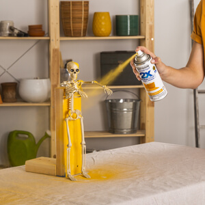 Applying Rust-Oleum 2X Ultra Cover Spray Paint in Gloss Golden Sunset to a plastic skeleton.