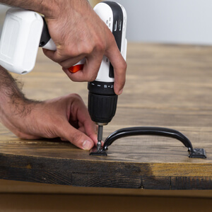 Man attaching metal handles to wood round fire pit cover with electric screw gun