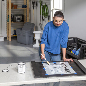 Woman using a paint brush and stencil to apply Rust-Oleum Chalked paint to noodle board.