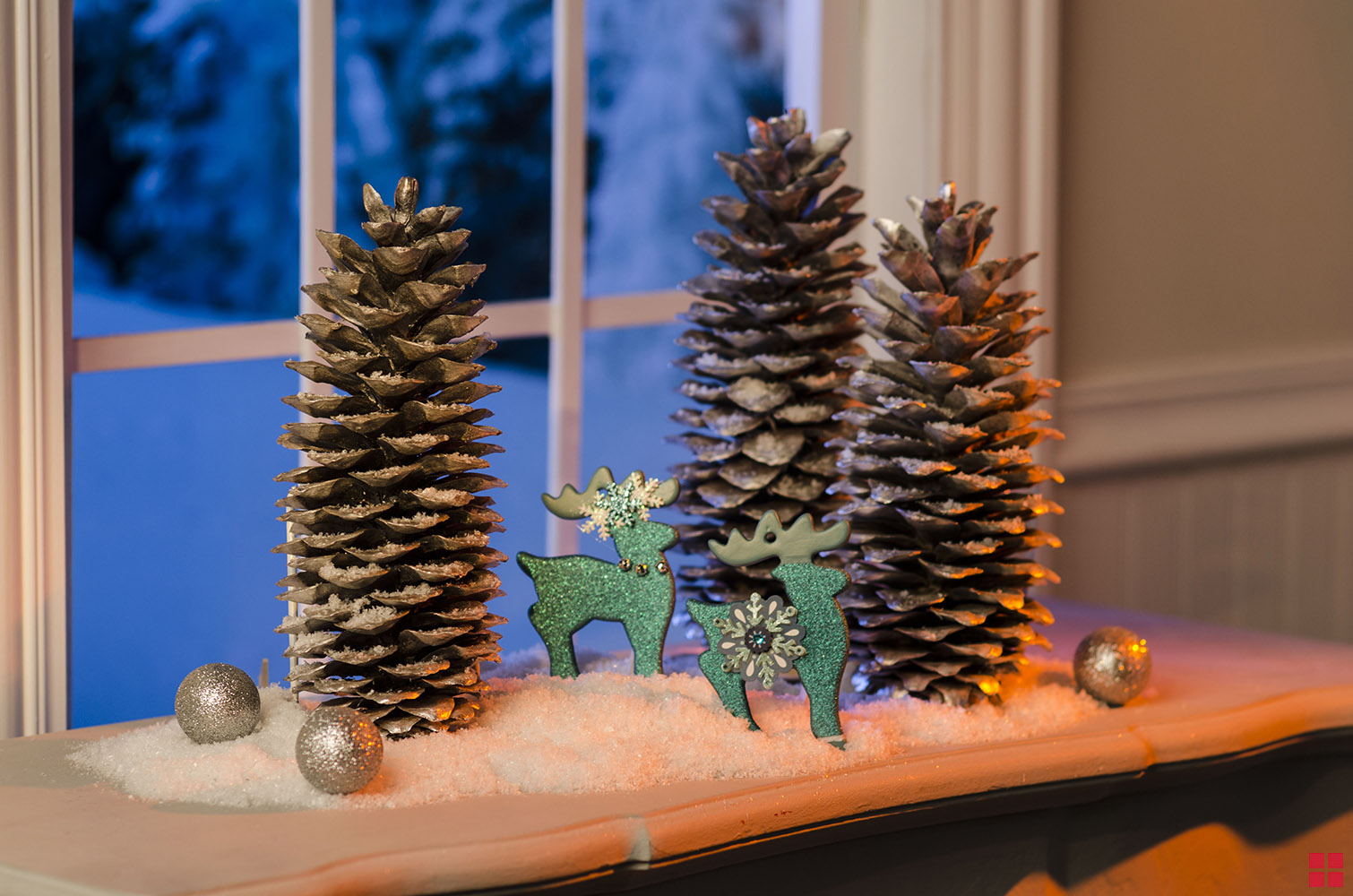 Glitter reindeer ornaments standing between pinecones in a holiday display.