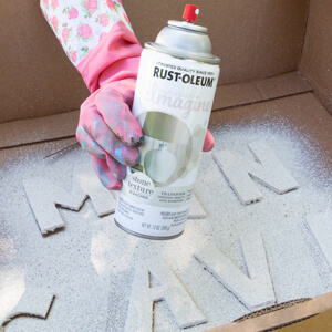 Holding a can of Rust-Oleum Imagine spray paint over “man cave” letters.