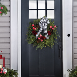 Green wreath with red pine cones and a black and white bow hanging on a front door.
