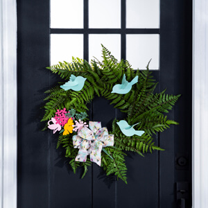 A green wreath with blue wooden birds and pink and yellow wooden flowers. 
