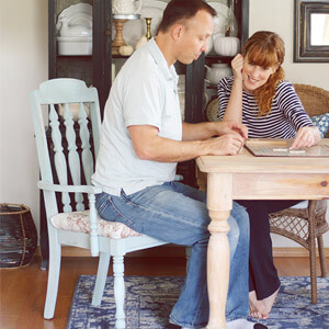 Man sitting on a pale blue chair while playing Scrabble with a woman. 