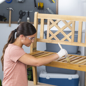 Woman applying Watco Teak Oil to wood bench.