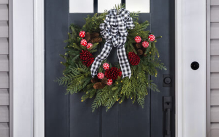 Green wreath with red pine cones and a black and white bow hanging on a front door.