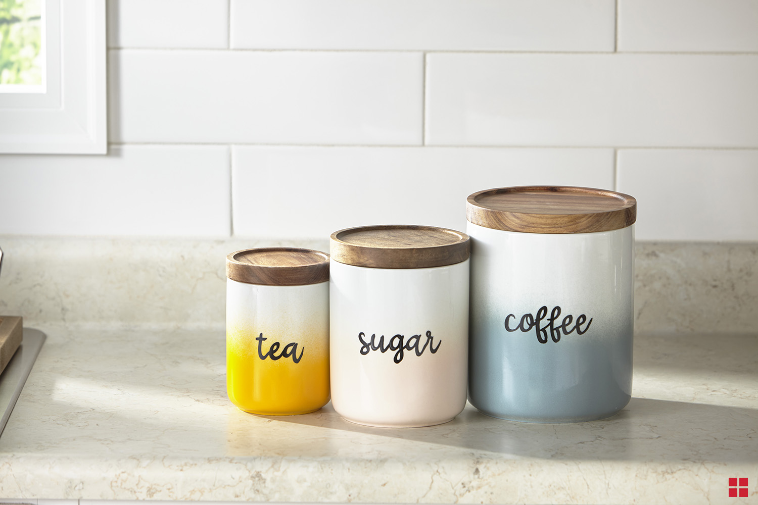Ombre painted canisters labeled tea, sugar and coffee on a kitchen counter.