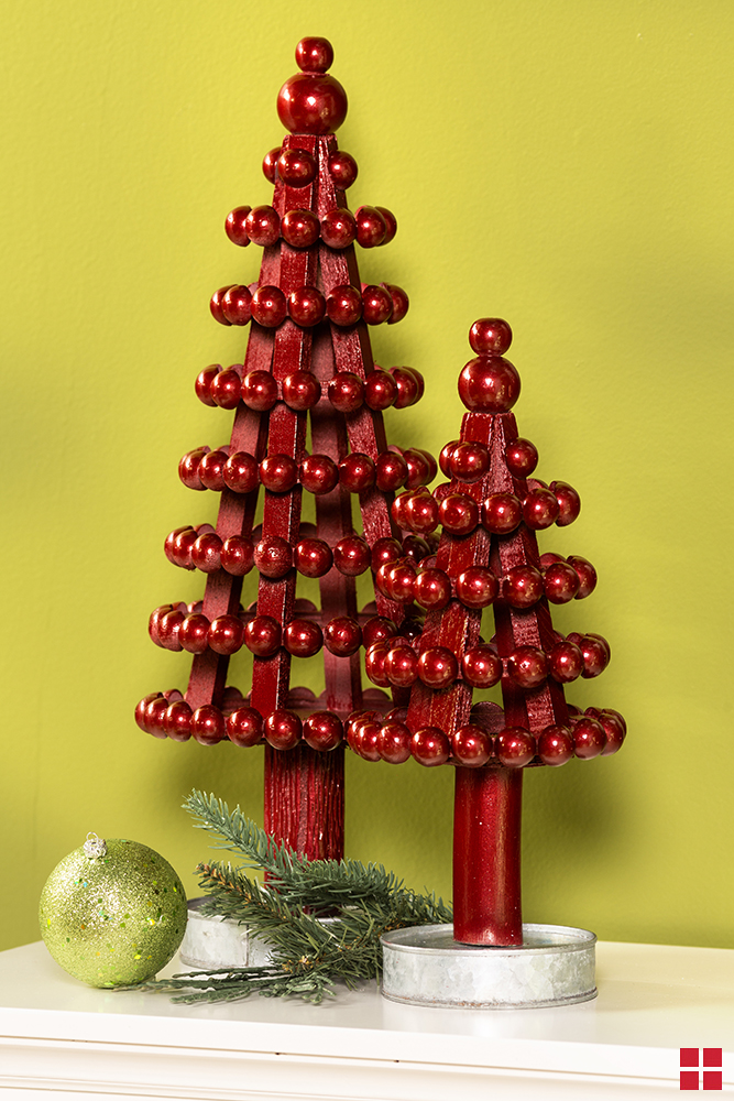 Two metallic red decorative trees on a white mantle with an evergreen sprig and green ornament below them.