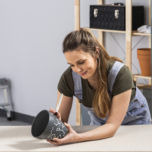 Woman drawing a design on painted flower pot with a Testors Paint Pen.