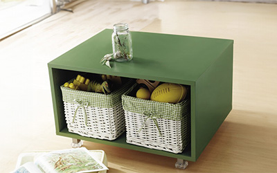 Green wooden storage box with two wicker baskets in it. 