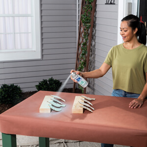 A woman applying blue spray paint to decorative wooden birds. 