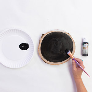 A hand applying Testors acrylic craft paint to birch wood slab. 