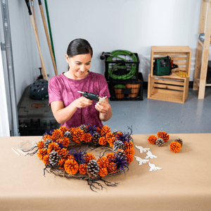 Woman gluing painted pinecones on a wreath.
