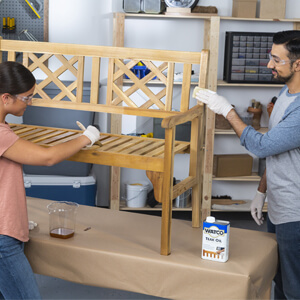 Man and woman applying Watco Teak Oil to wood bench.