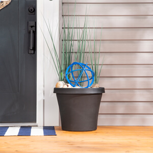 An urn planter filled with green grass, seashells and a blue orb next to a front door. 
