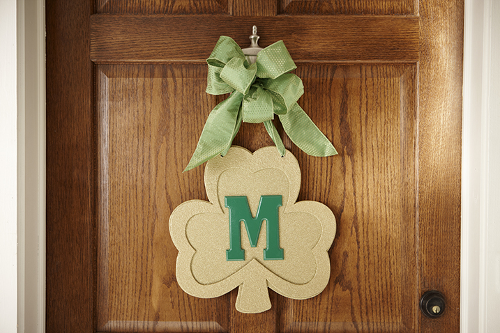 Wooden shamrock door decoration with a green M in the center. 