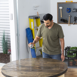 Man spraying spar urethane protective coat to stained wood round