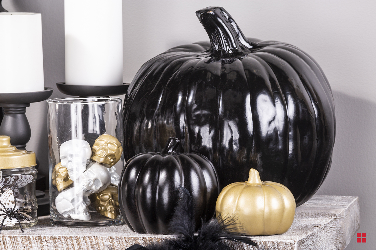 Decorative pumpkins painted black and gold next to a jar full of small decorative painted skulls.