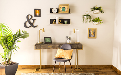 A home office with a desk, chair and potted palm tree and shelves, pictures and planters hanging from the wall. 