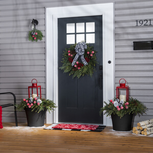 A front porch with black planters filled with wreaths and red lanterns on either side of the door. 