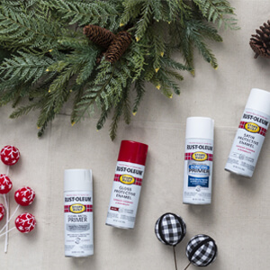 Greenery, pine cones, artificial berries, a black lantern with a candle inside and four cans of Rust-Oleum Stops Rust spray paint and primer. 