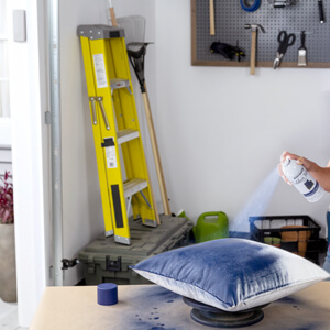 Woman spraying Rust-Oleum Outdoor Fabric Paint on a throw pillow
