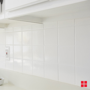 A white tile backsplash between an off-white countertop and white upper cabinets.