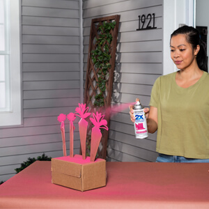 A woman applying pink 2X Ultra Cover spray paint to decorative wooden flowers. 