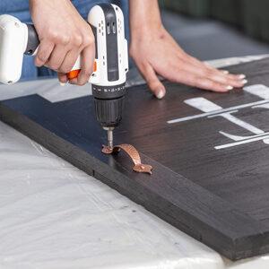 Woman’s hand using drill to attach handle to a noodle board.