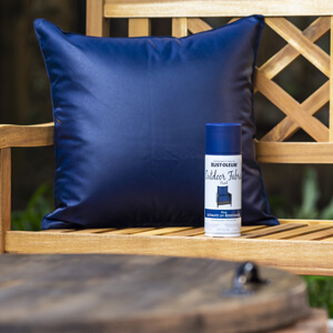 Painted throw pillow with can of Rust-Oleum Outdoor Fabric paint on a bench