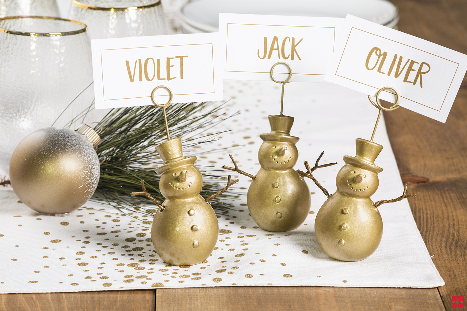 Closeup view of three gold snowman place card holders with cards reading Violet, Jack and Oliver.