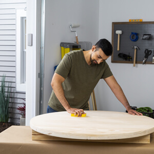 Man sanding round wood fire pit cover