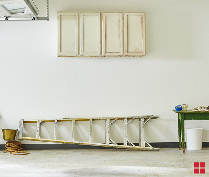 A garage with a ladder laying on the ground and a bank of four unpainted wood cabinets on the wall.