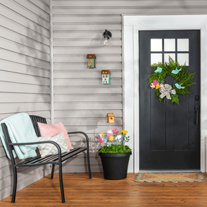 Colorful wooden flowers and small birdhouses in two urn planters placed on either side of the front door. 
