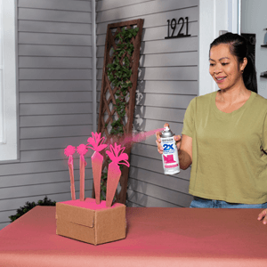 A woman applying bright pink spray paint to decorative wooden flowers.