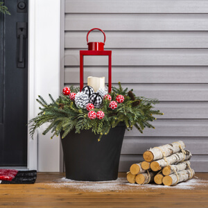 Black planter filled with greenery, pine cones and a red lantern.