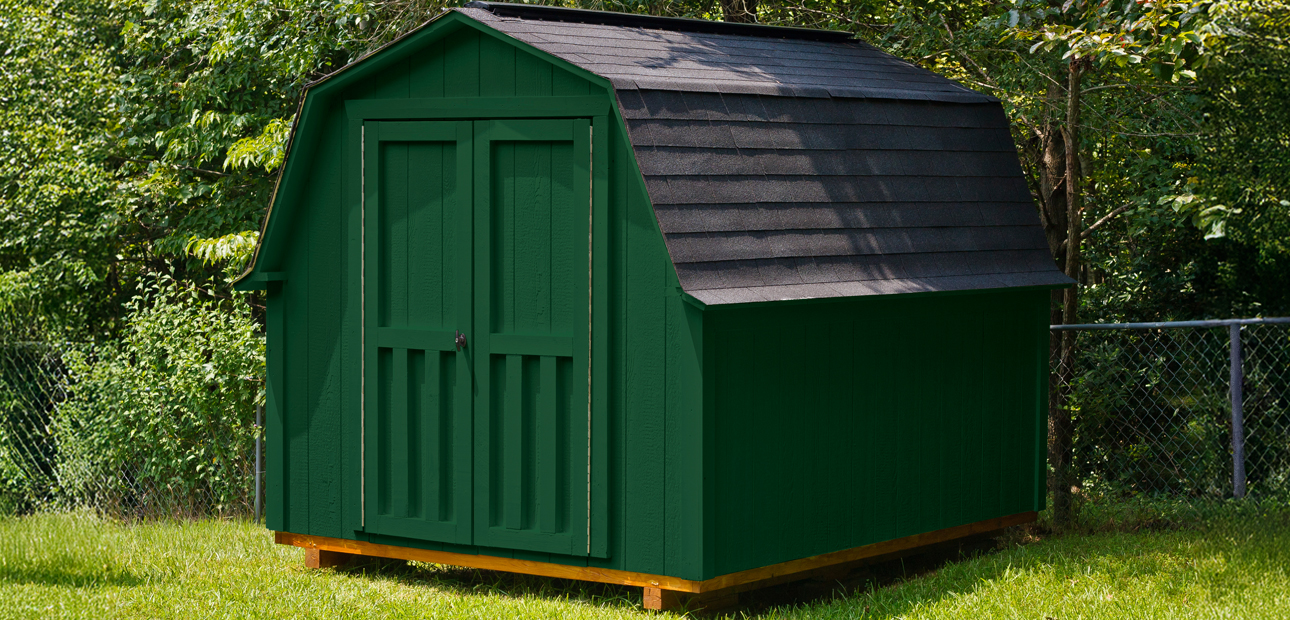  A green storage shed in front of green, leafy trees.