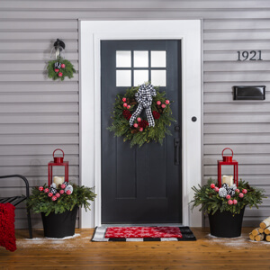 A front porch with a green wreath with red pine cones and a black and white bow hanging on a front door.
