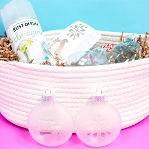 Two frosted glass ornaments in front of a basket containing Rust-Oleum Imagine Spray Paint and craft supplies. 